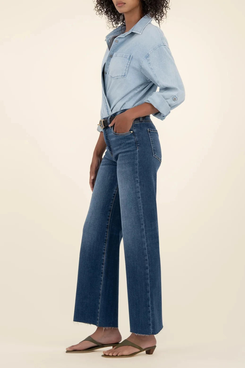 Person wearing a light blue denim shirt and dark blue jeans on a beige background
