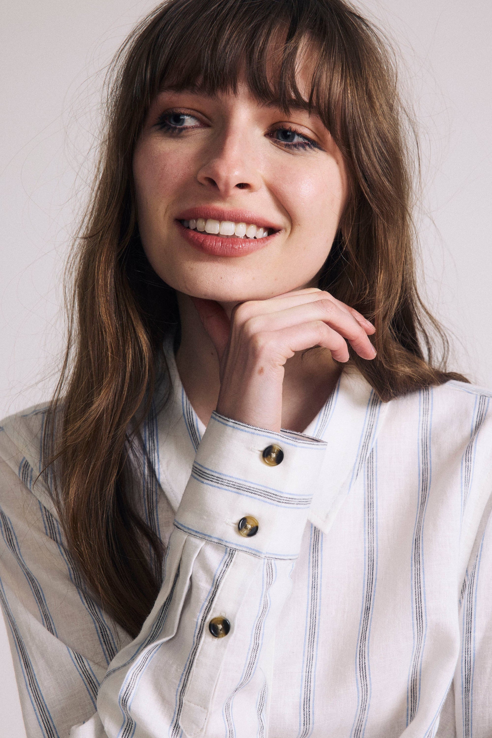 Woman wearing a white and gray striped shirt with a neutral background