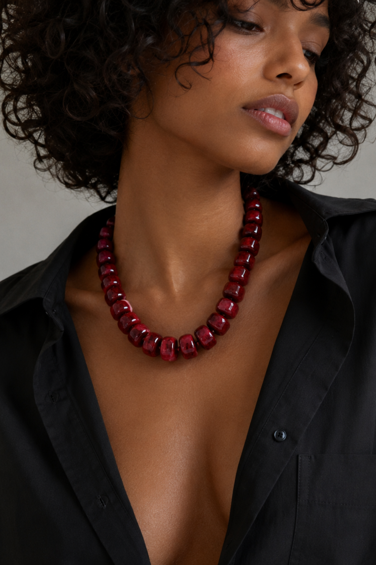 Woman wearing a red beaded necklace with a black shirt against a neutral background