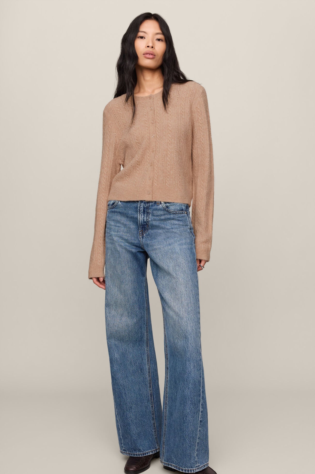 Woman wearing a beige sweater and blue jeans on a plain background