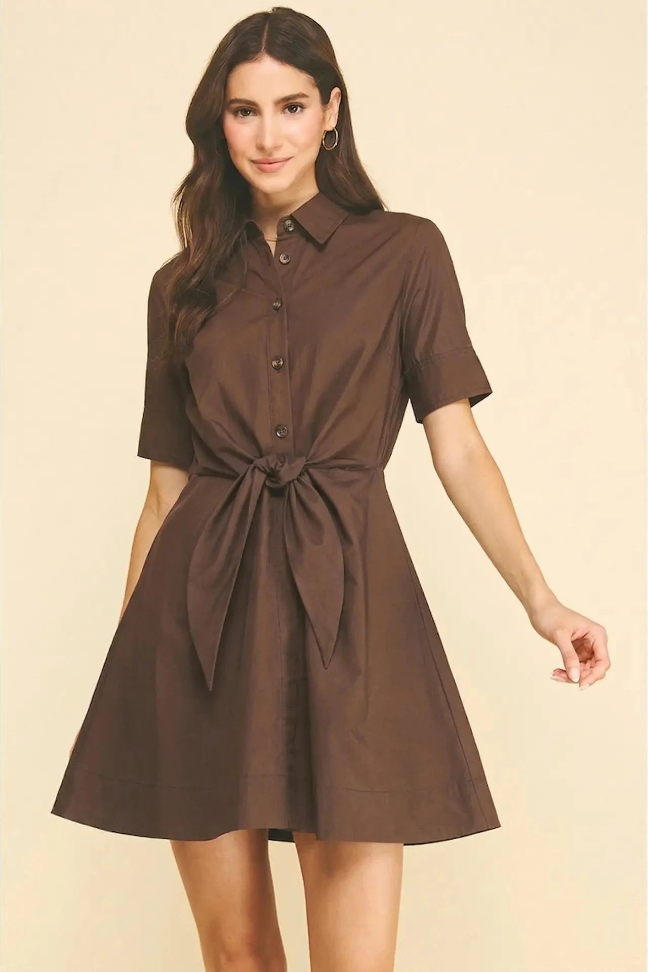 Woman wearing a brown dress with a belt on a beige background