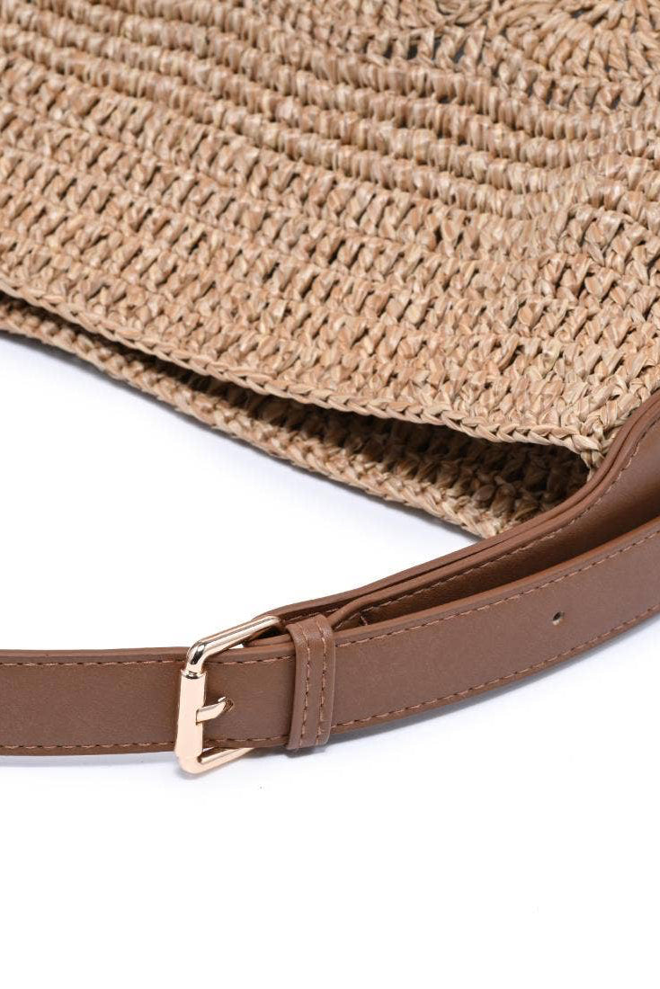 Woven straw bag with a brown leather strap on a white background
