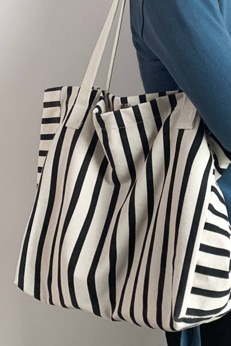 Person holding a black and white striped tote bag against a neutral background