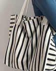 Person holding a black and white striped tote bag against a neutral background