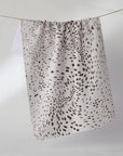 A white cotton kitchen towel with a black spotted dalmatian-style pattern, hanging from a thin wire on a plain white background.