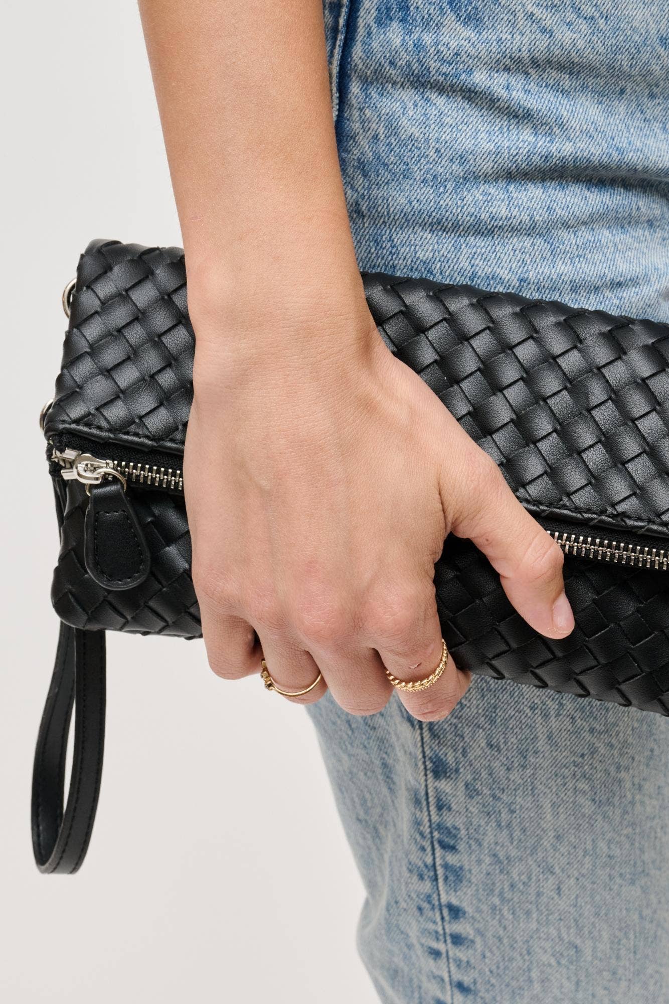 Person holding a black woven clutch bag with a plain background