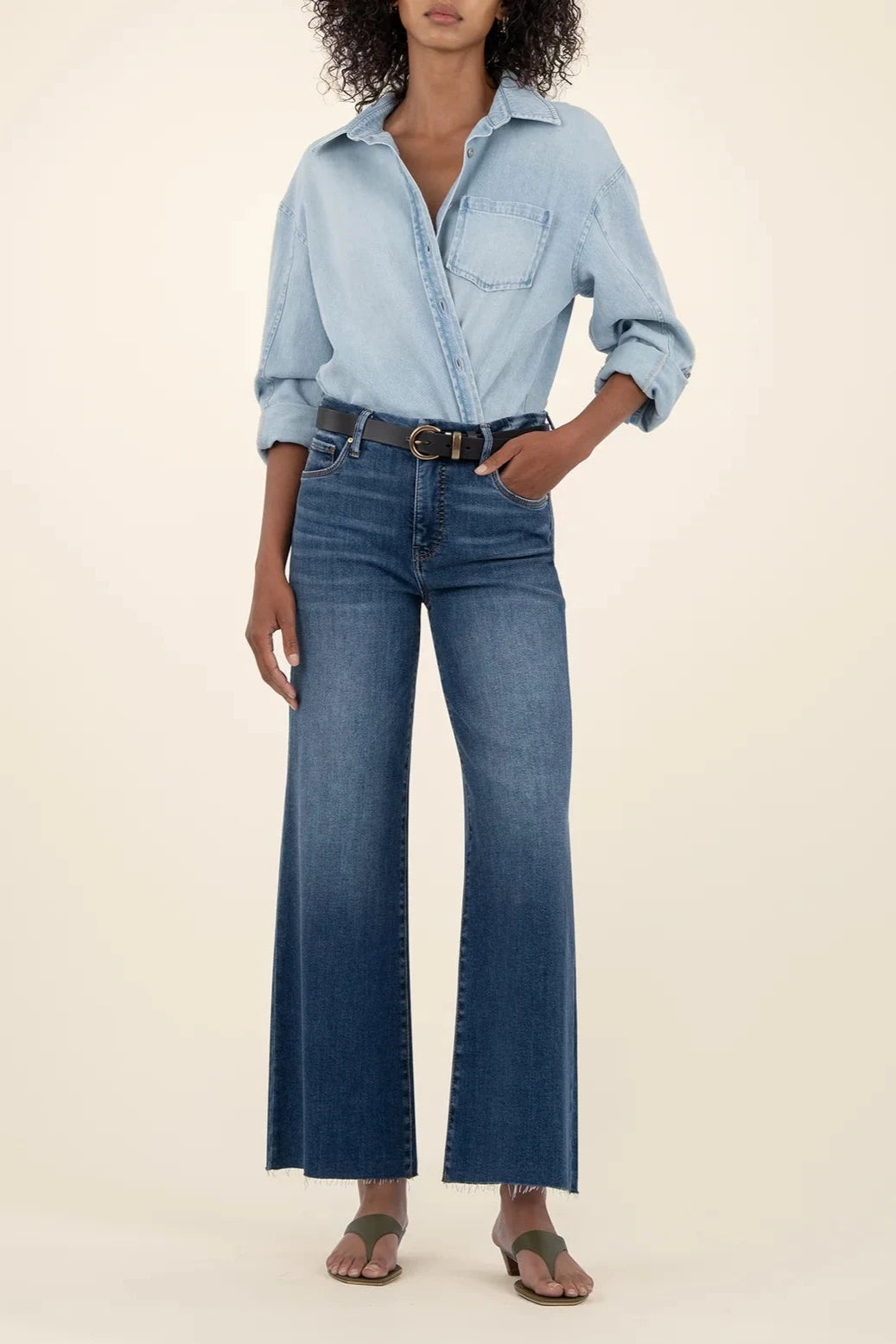 Person wearing a light blue denim shirt and dark blue jeans on a beige background