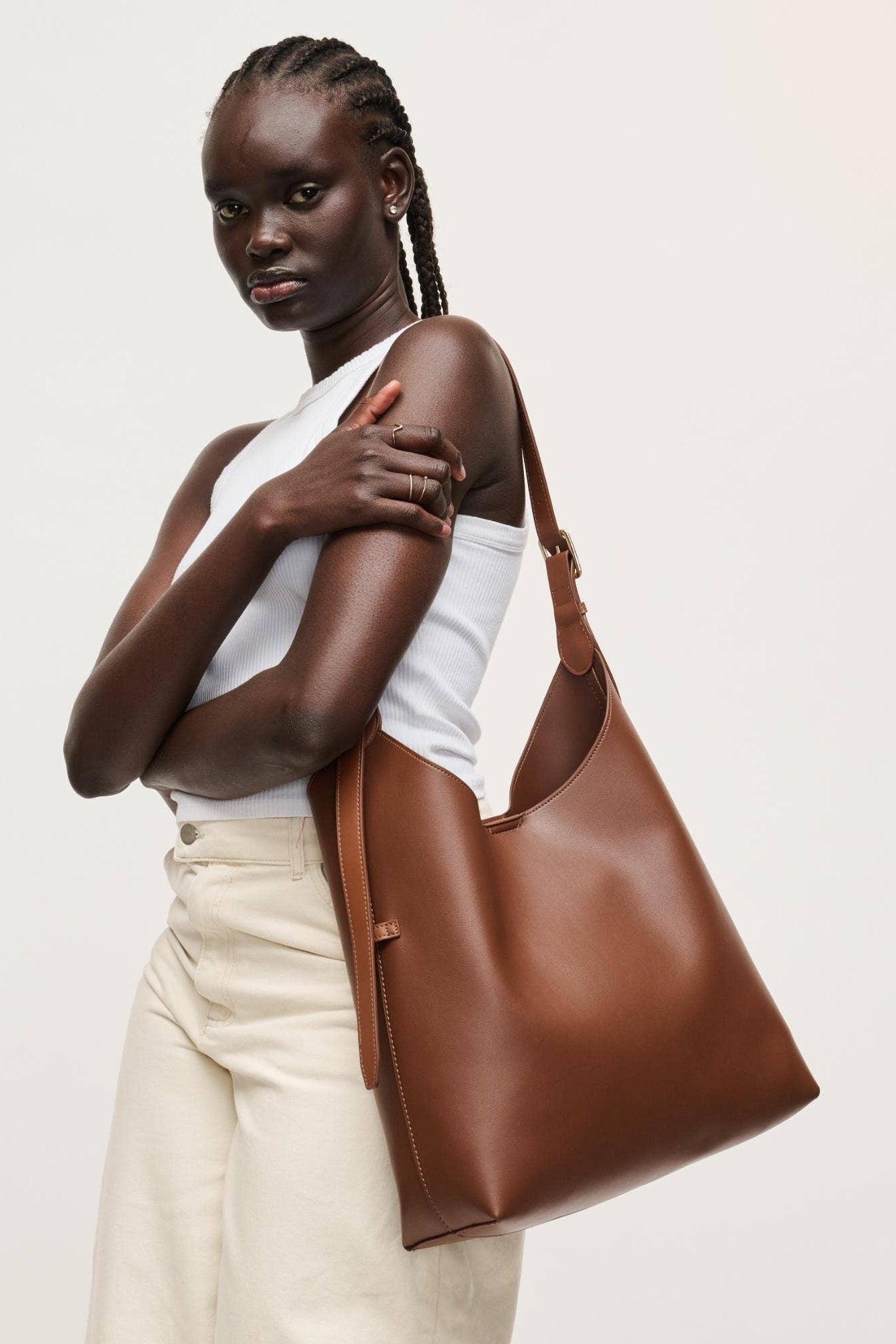 Woman holding a brown leather handbag against a plain background