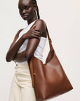Woman holding a brown leather handbag against a plain background