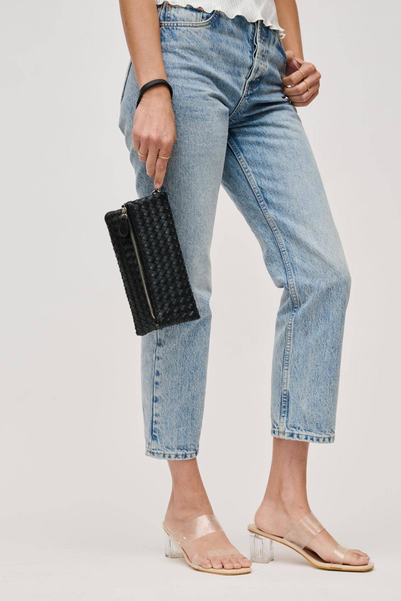 Person wearing light blue jeans holding a black clutch against a plain background