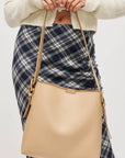 Beige handbag held by a person wearing a plaid skirt and cream sweater on a light gray background