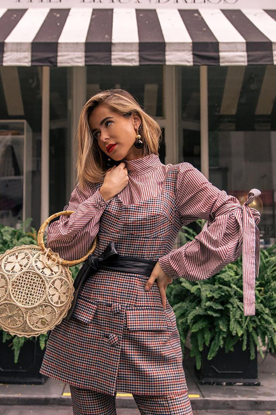 Woman in a checkered outfit holding a round woven bag in front of &#39;The Laundress&#39; store.