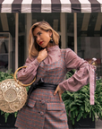 Woman in a checkered outfit holding a round woven bag in front of 'The Laundress' store.