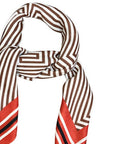 A patterned silk scarf with brown and white geometric stripes and red chevron ends, styled in a loop on a plain white background.