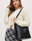 Woman holding a black handbag against a plain background