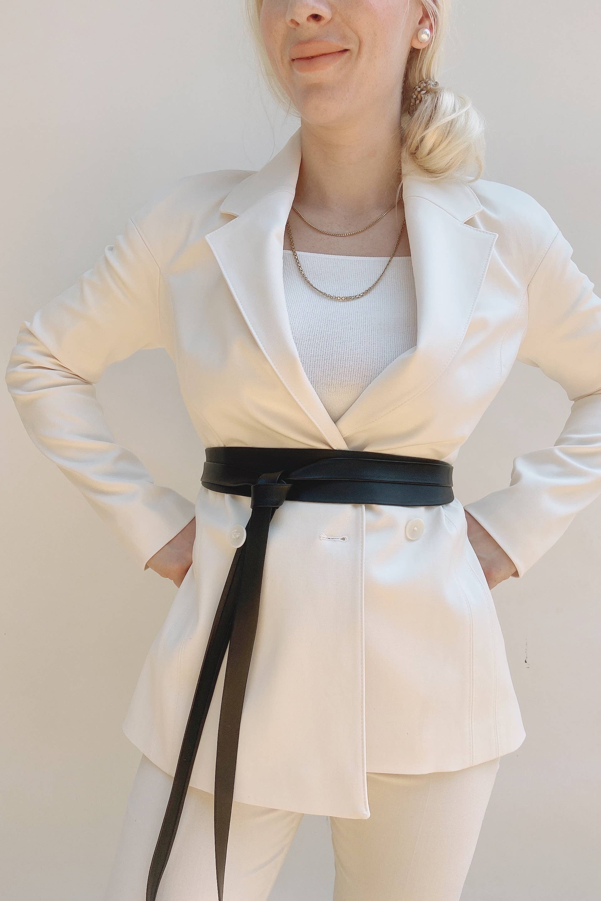 Person wearing a white blazer with a black belt against a plain background