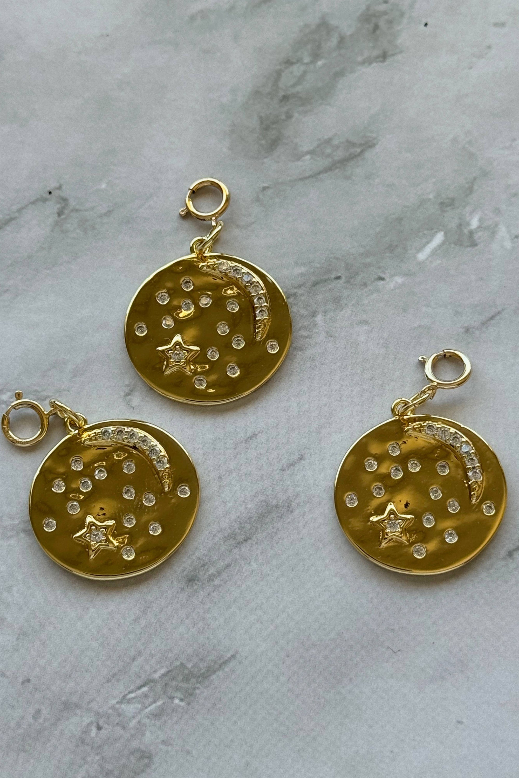 Gold circular pendants with star and moon designs on a marble surface