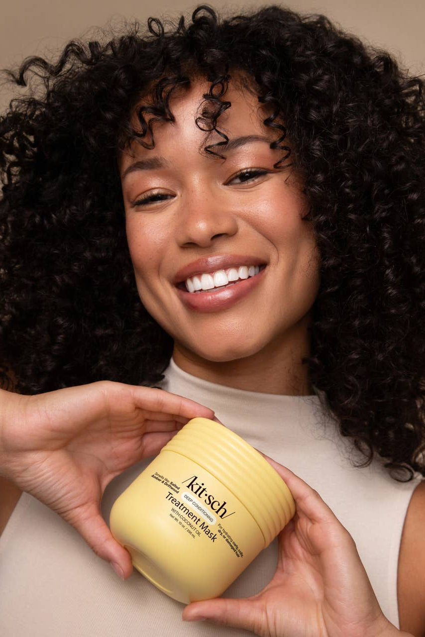 Woman holding a jar of 'Kitsch' hair mask against a beige background
