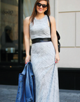 Woman in a long light gray dress with a black belt, standing outdoors.