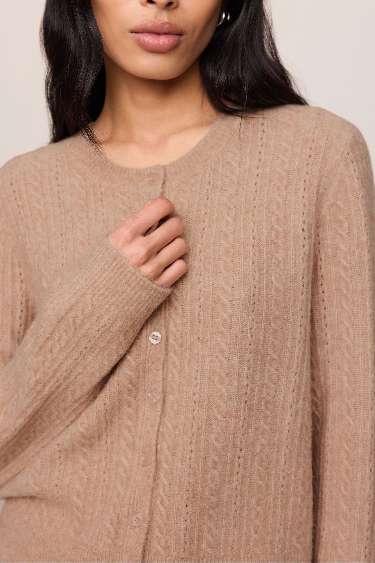 Close-up of a person wearing a beige cable knit sweater against a neutral background