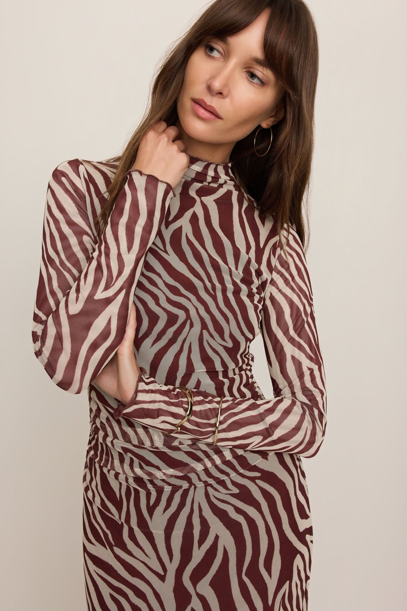 A woman wearing a long-sleeve mock-neck dress with a brown and beige zebra print pattern, posed against a solid light beige background.