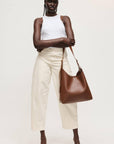 Woman holding a brown leather bag against a plain background