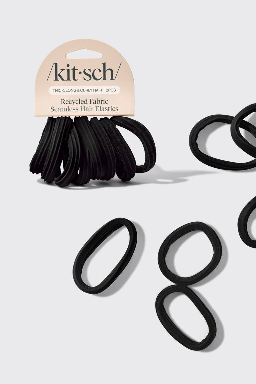 A pack of black Kit-Sch seamless hair elastics with a cardboard header, shown alongside several loose oval-shaped black elastics on a light gray background.