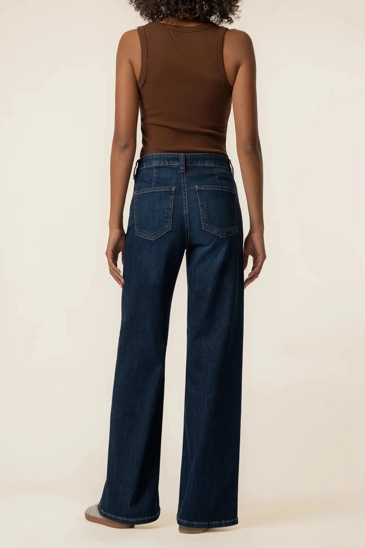 A model shown from the back wearing dark blue wide-leg jeans and a brown ribbed tank top, standing against a plain beige studio background.