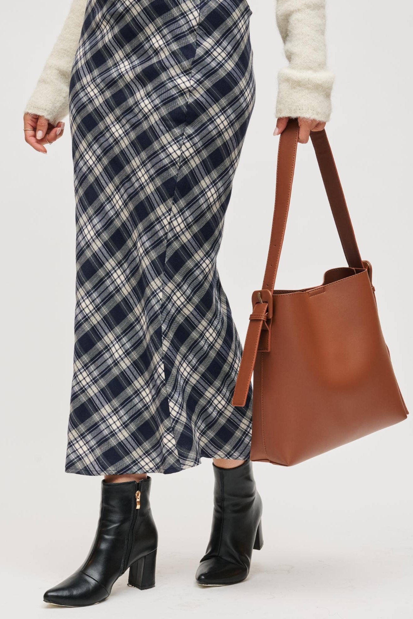 Person wearing a plaid skirt and holding a brown leather bag on a white background