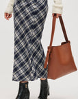 Person wearing a plaid skirt and holding a brown leather bag on a white background