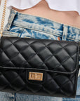 Black quilted handbag with gold chain strap held by a person wearing a white shirt and blue jeans.
