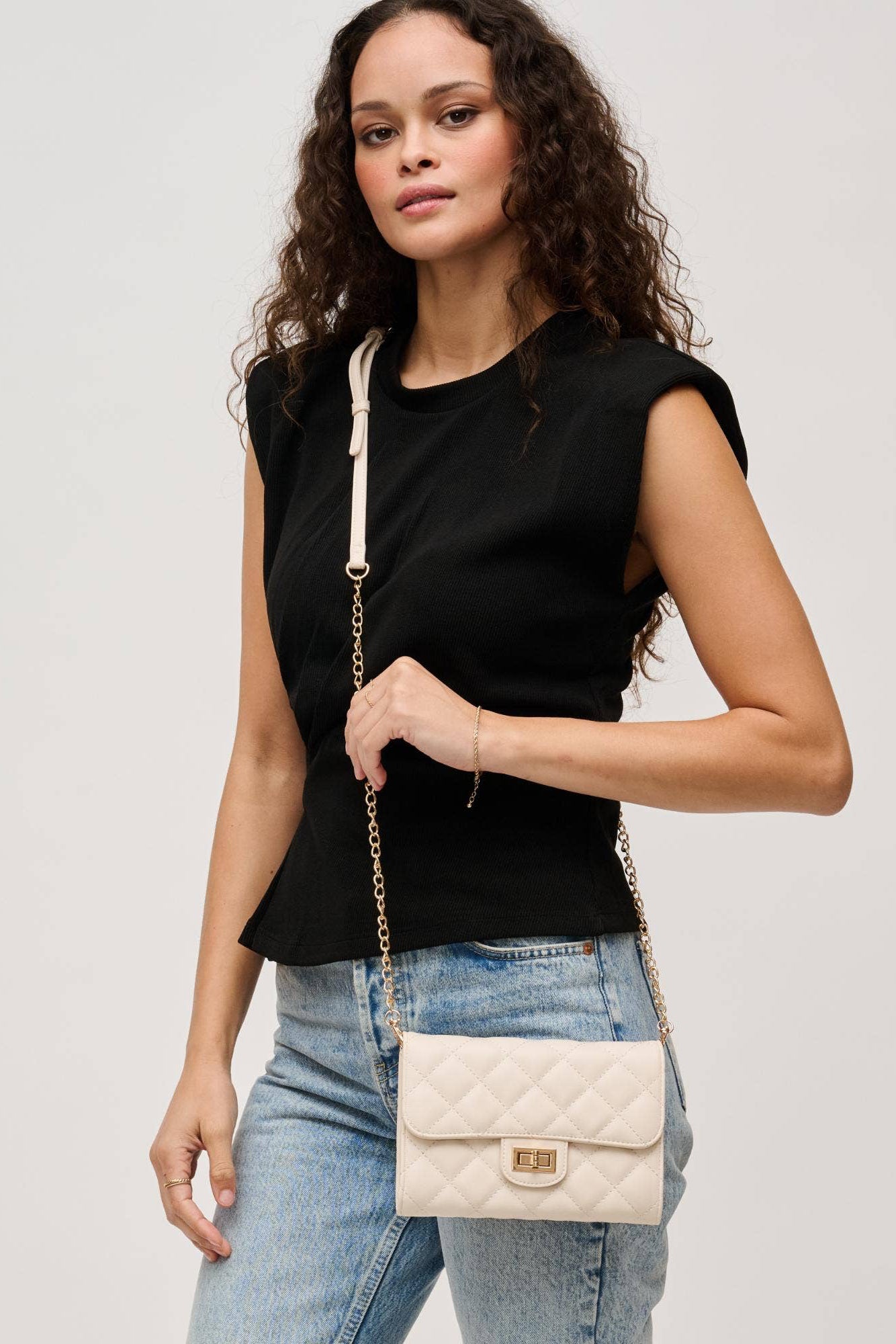 Woman holding a white quilted handbag against a plain background