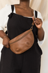 Person wearing a brown leather crossbody bag against a neutral background