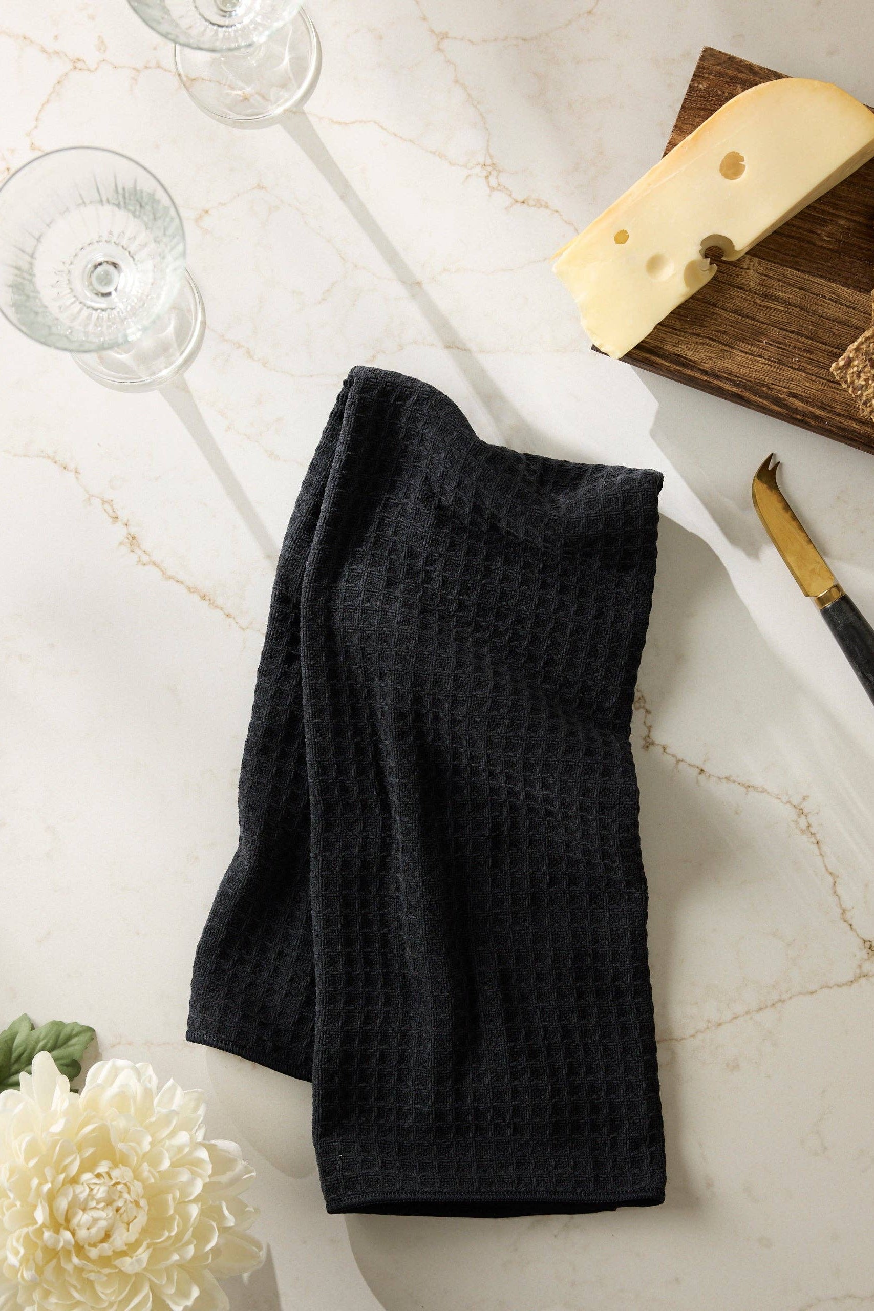 Black folded towel on a marble surface with a glass, cheese, and crackers.