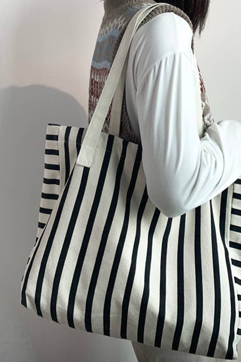 Person holding a black and white striped tote bag against a plain background