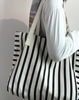 Person holding a black and white striped tote bag against a plain background