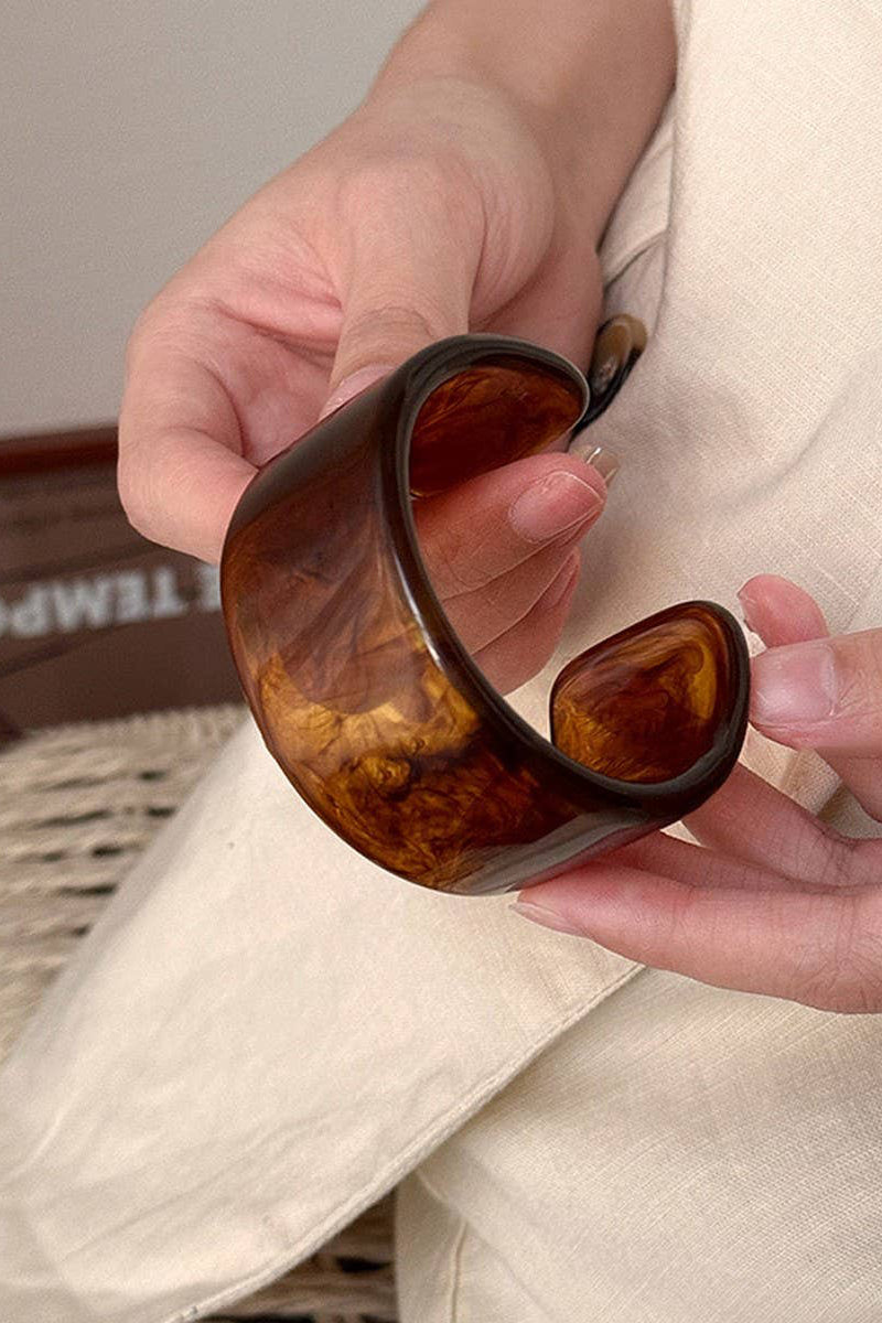 Person holding a pair of sunglasses with tortoiseshell frame and brown lenses.