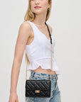 Woman wearing a white top and blue jeans with a black quilted handbag on a light gray background
