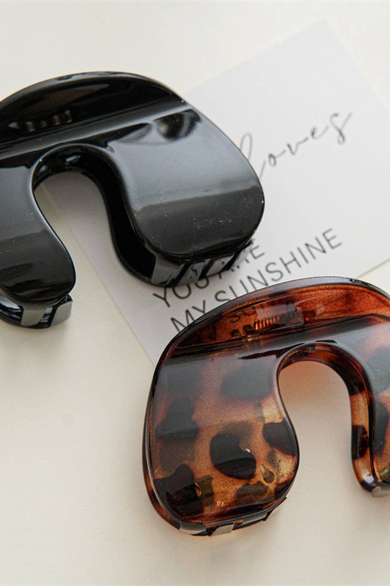 Black and tortoiseshell hair clip on a light surface with text in the background