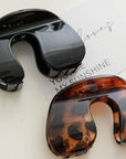 Black and tortoiseshell hair clip on a light surface with text in the background