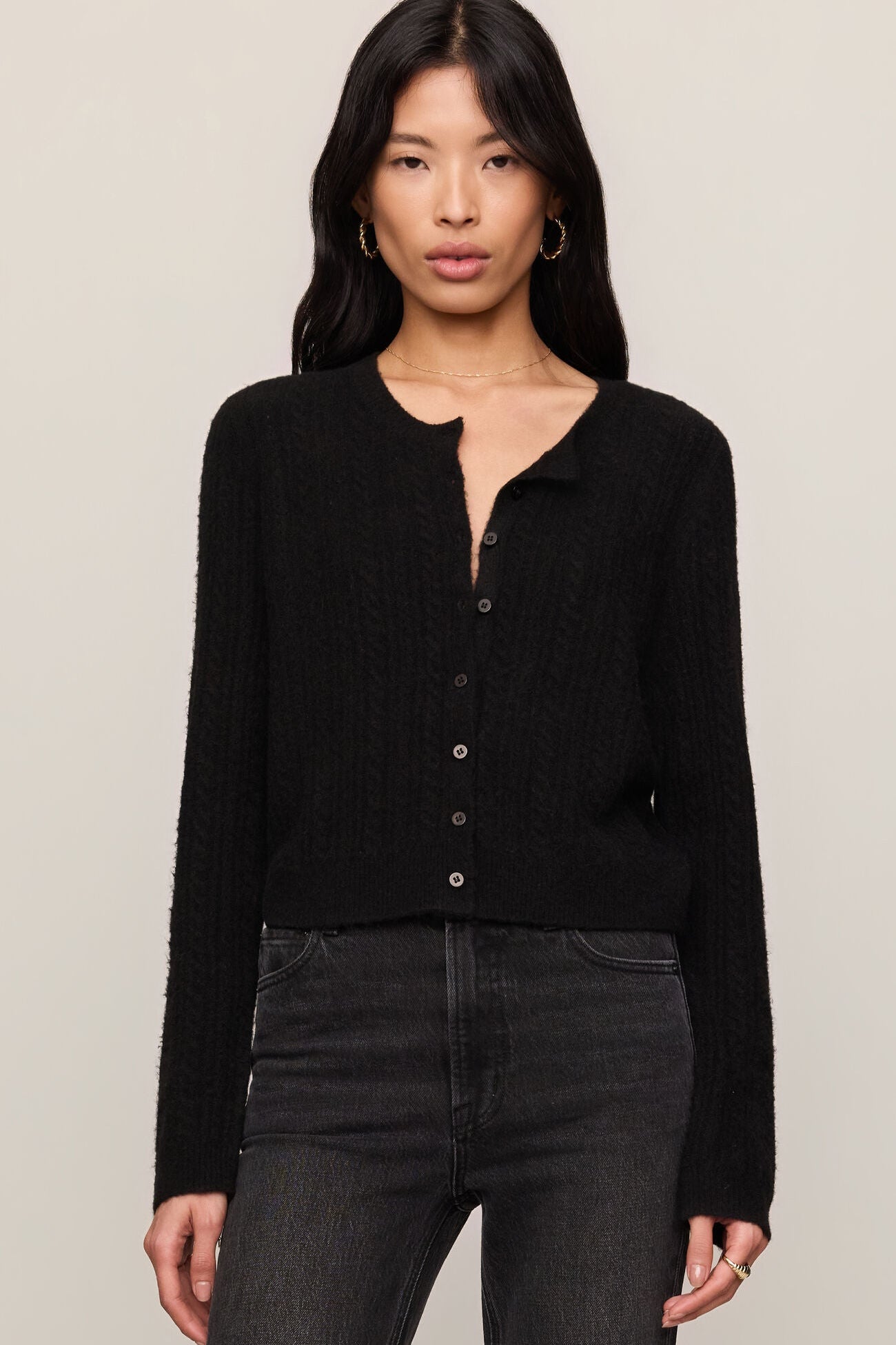 Woman wearing a black cardigan and dark jeans against a plain background