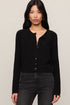 Woman wearing a black cardigan and dark jeans against a plain background