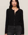 Woman wearing a black cardigan and dark jeans against a plain background