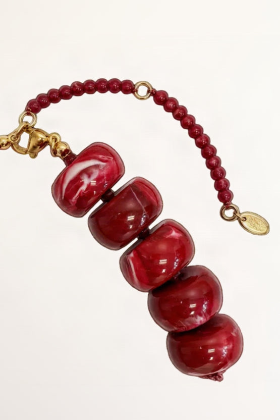 Red beaded bracelet with gold accents on a white background