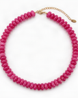 A chunky beaded necklace made of faceted hot pink beads, completed with a delicate gold chain extender and clasp, shown on a plain white background.
