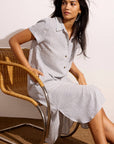 Woman wearing a light gray dress sitting on a wicker chair against a white wall.