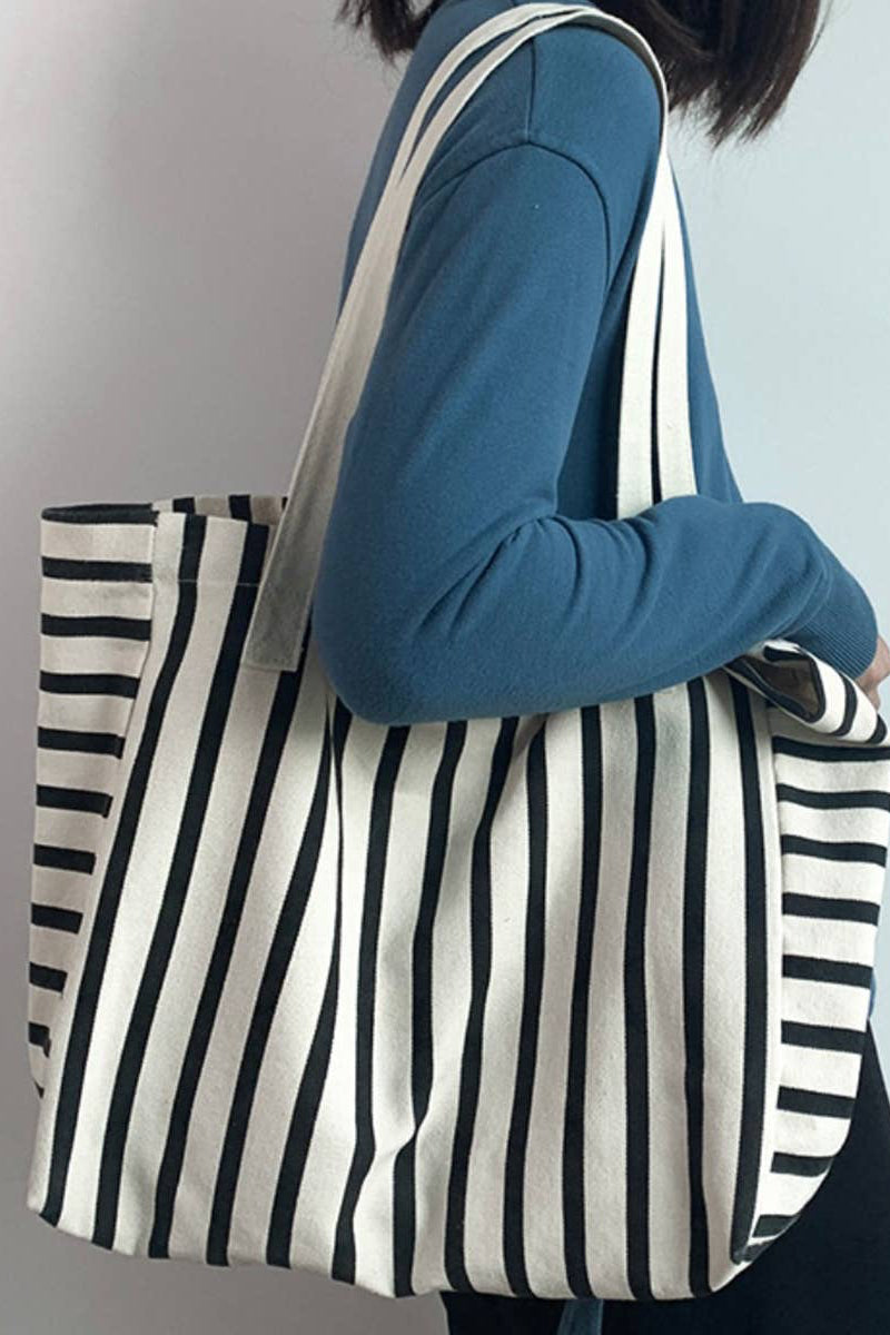 Person holding a black and white striped tote bag against a plain background