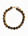 A beaded necklace made of polished tiger's eye beads with gold spacer rings and a gold chain clasp, displayed on a clean white background.