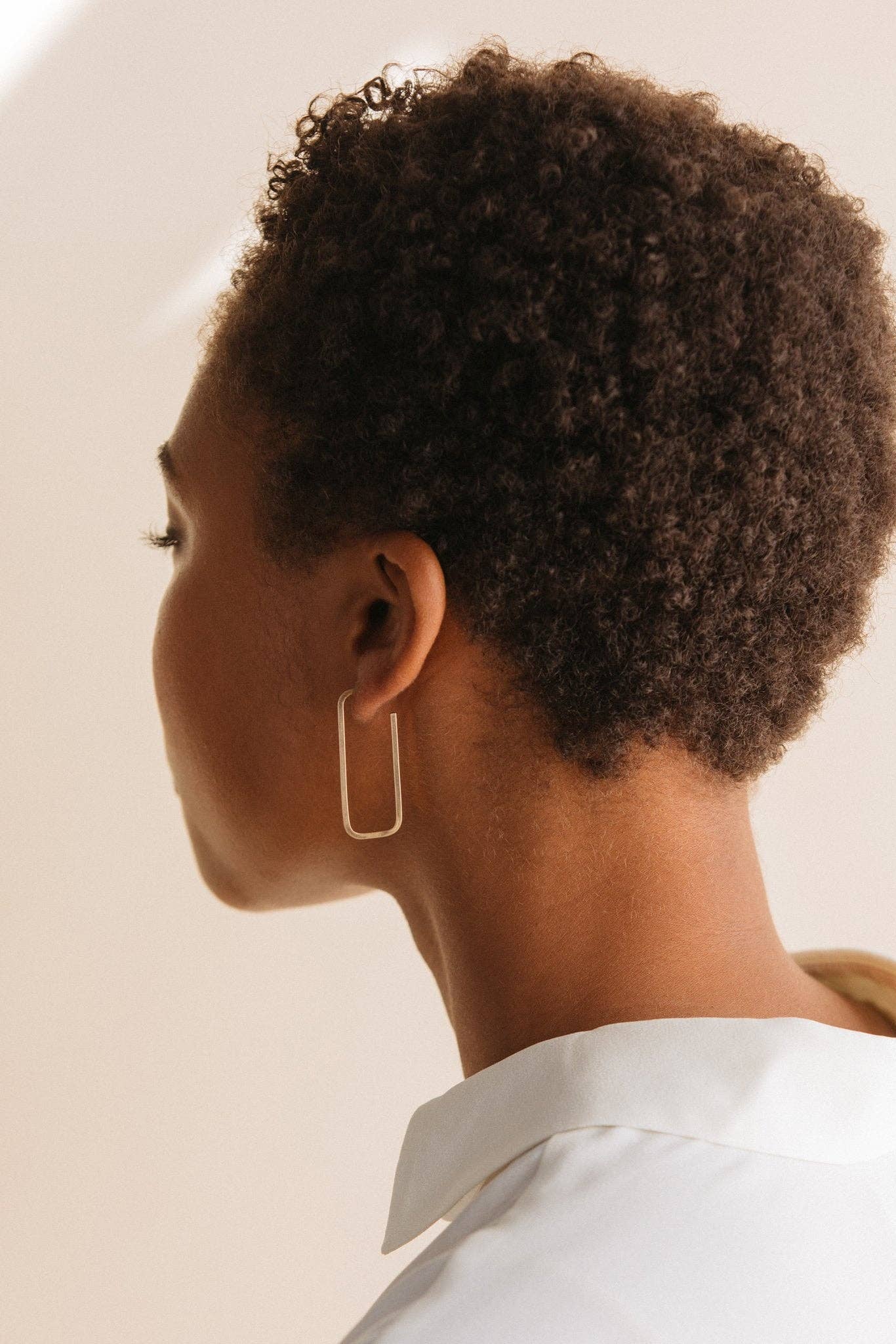 Person with short, curly hair wearing a gold hoop earring against a neutral background
