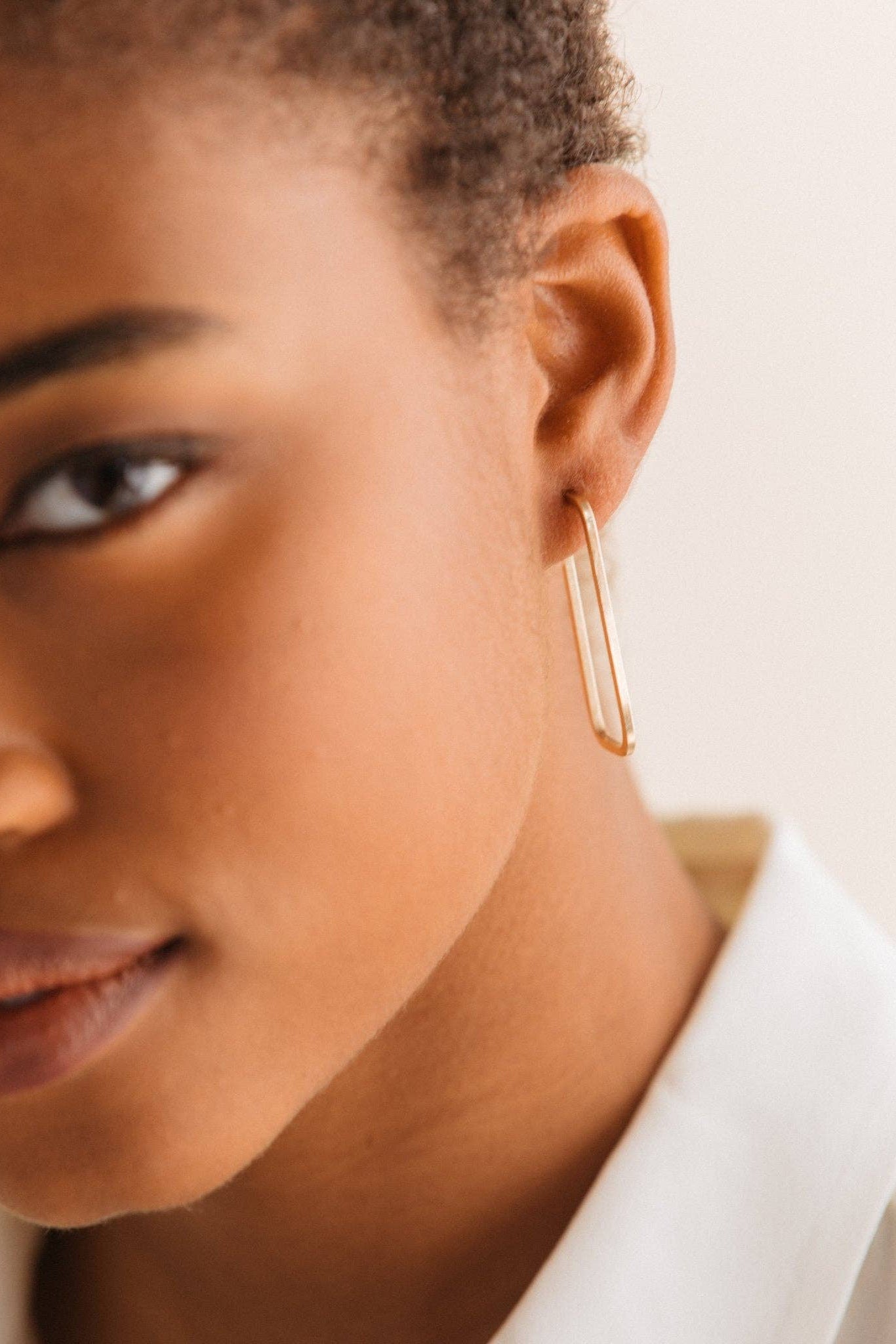 Close-up of a person wearing a gold hoop earring with a neutral background